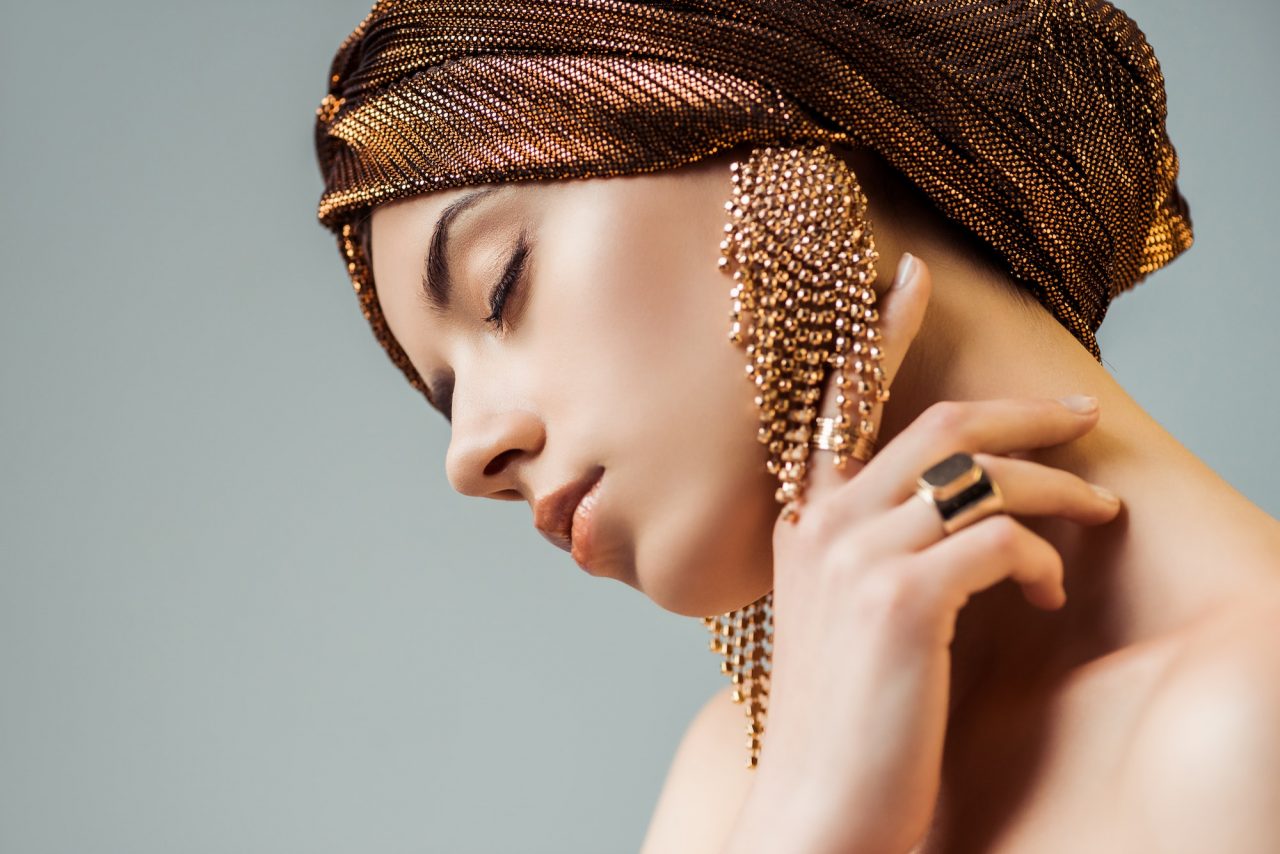 young-nude-woman-with-closed-eyes-shiny-makeup-golden-rings-and-earrings-in-turban-touching-neck.jpg